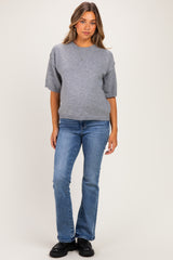 woman wearing a grey maternity sweater and blue flared jeans, with no visible baby bump