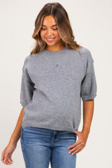 woman wearing a grey short sleeve maternity sweater and blue jeans, smiling with a relaxed fit