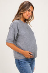 woman wearing a gray short sleeve maternity sweater and holding her baby bump