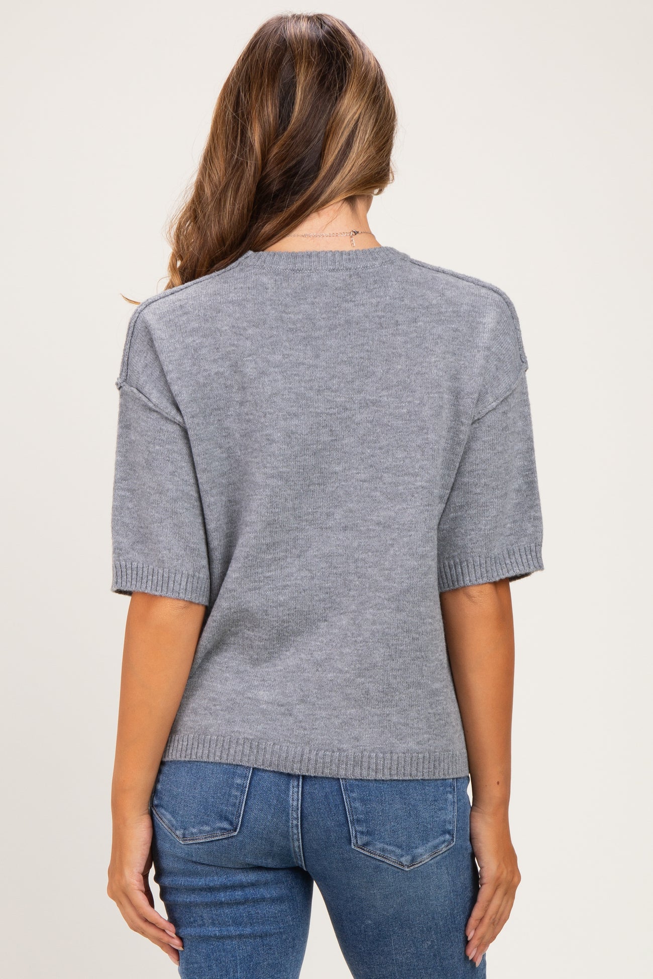woman wearing a gray short sleeve maternity sweater, styled with a relaxed fit and ribbed hem, viewed from the back