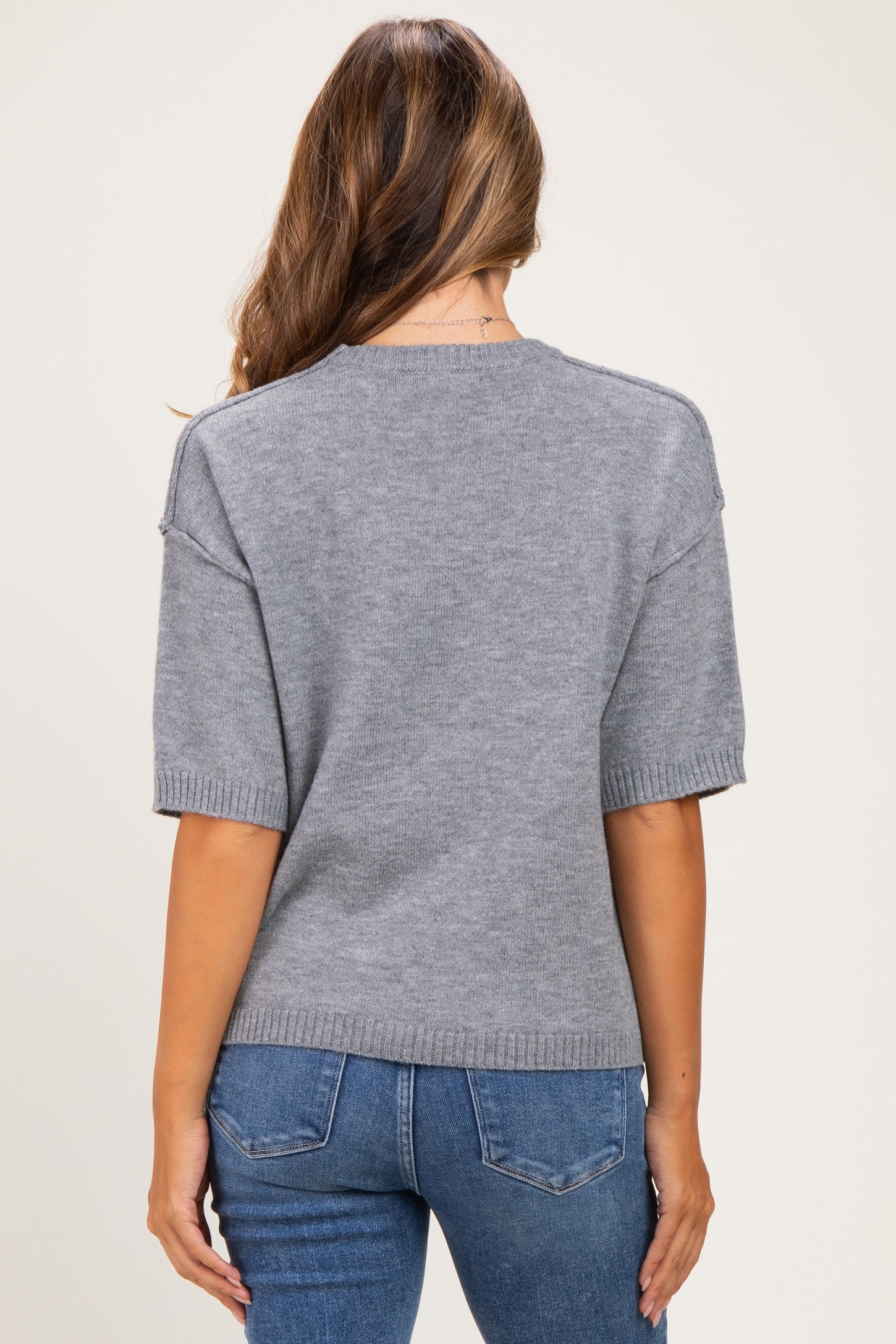 woman wearing a gray short sleeve maternity sweater, styled with a relaxed fit and ribbed hem, viewed from the back