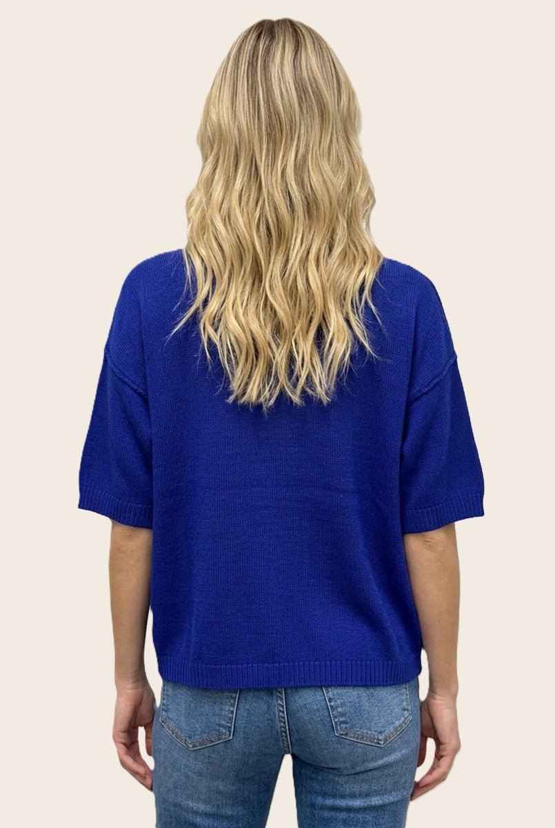woman wearing a short sleeve bright blue sweater with a relaxed fit, showing the back view and paired with light blue jeans