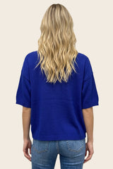 woman wearing a short sleeve bright blue sweater with a relaxed fit, showing the back view and paired with light blue jeans
