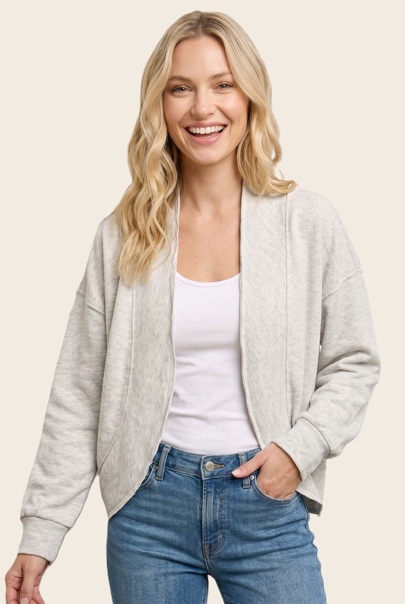 woman wearing a light gray bomber-style cardigan over a white top and blue jeans, smiling at the camera