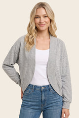 woman wearing a light gray cropped cardigan over a white tank top and blue jeans