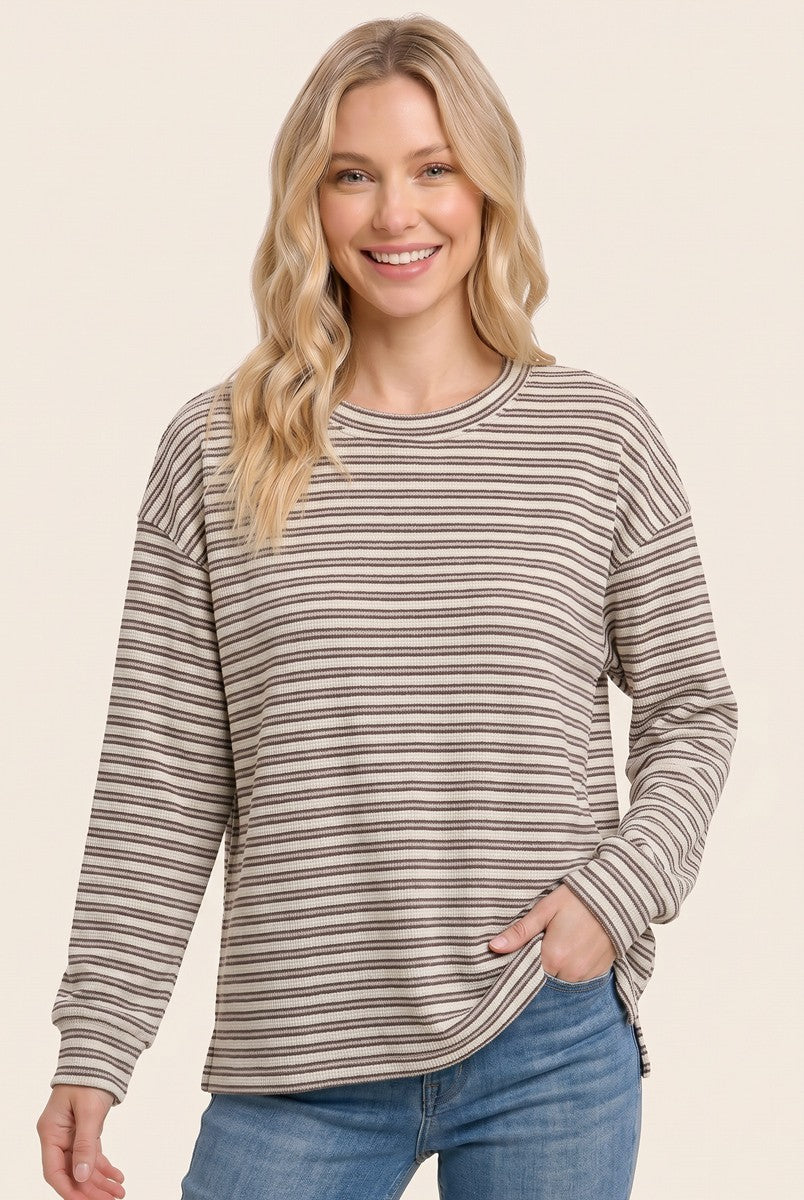 woman wearing a beige and brown striped long sleeve top with side slits and relaxed fit, smiling at the camera