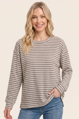 woman wearing a beige and brown striped long sleeve top with side slits and relaxed fit, smiling at the camera