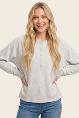 woman wearing a light gray long sleeve henley top with button details and relaxed fit, smiling with hands on hips