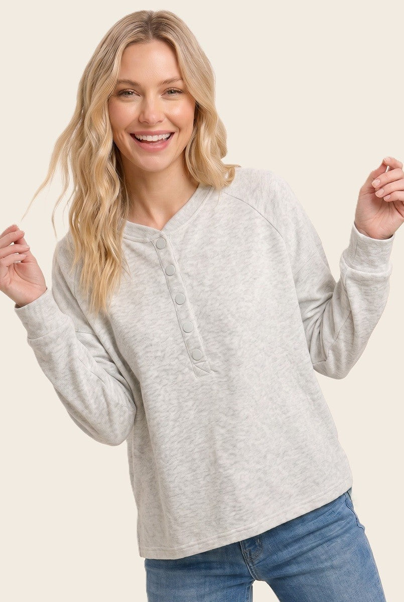 woman wearing a light gray long sleeve button-up top with a relaxed fit and round neckline