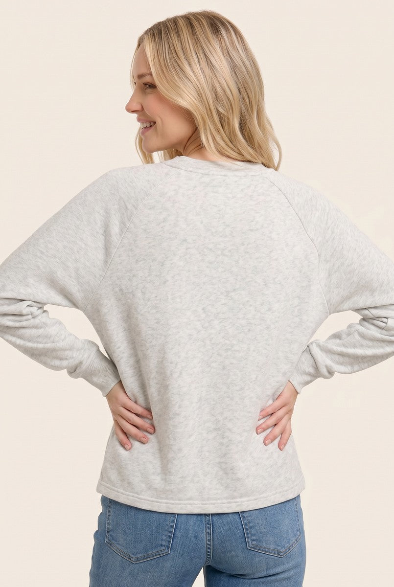 woman wearing a light gray raglan sleeve sweatshirt with a relaxed fit, standing with hands on hips