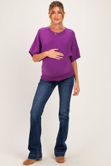 woman wearing a purple maternity sweater and blue flared jeans, gently cradling her baby bump