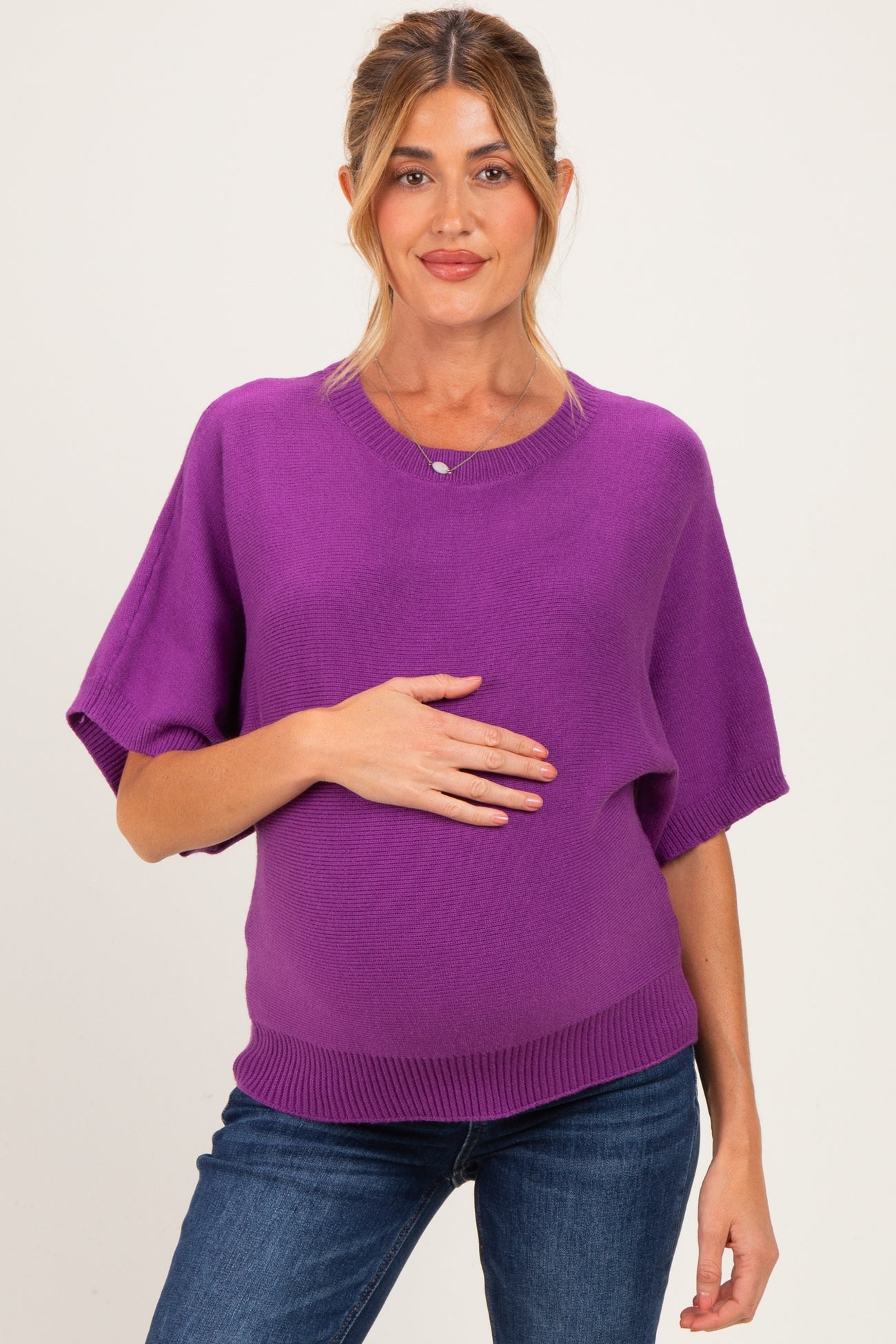 woman wearing a purple short sleeve maternity sweater and holding her baby bump