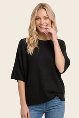 woman wearing a black oversized knit sweater and smiling with casual blue jeans