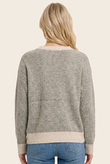 woman wearing a gray and beige striped sweater with a loose fit and long sleeves, viewed from the back