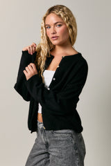 woman wearing a black cardigan over a white top and gray high-waisted jeans, with wavy blonde hair