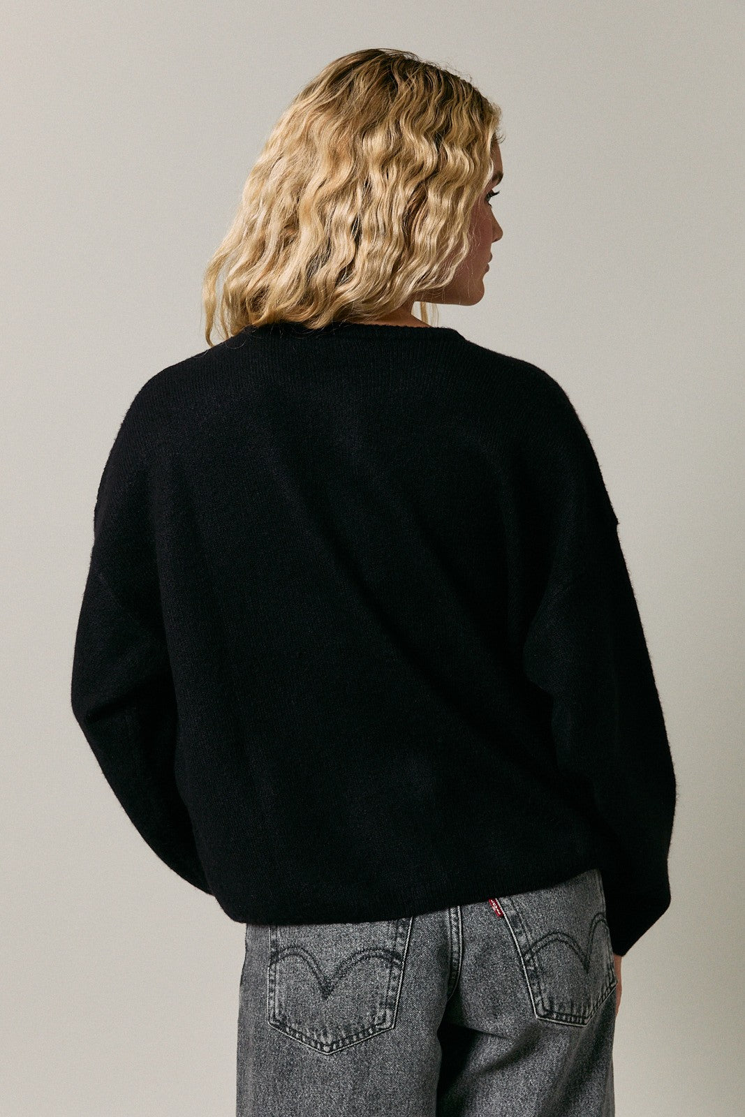 woman wearing a black oversized sweater with a relaxed fit, styled with gray jeans, viewed from the back