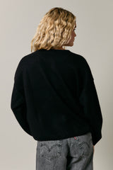 woman wearing a black oversized sweater with a relaxed fit, styled with gray jeans, viewed from the back