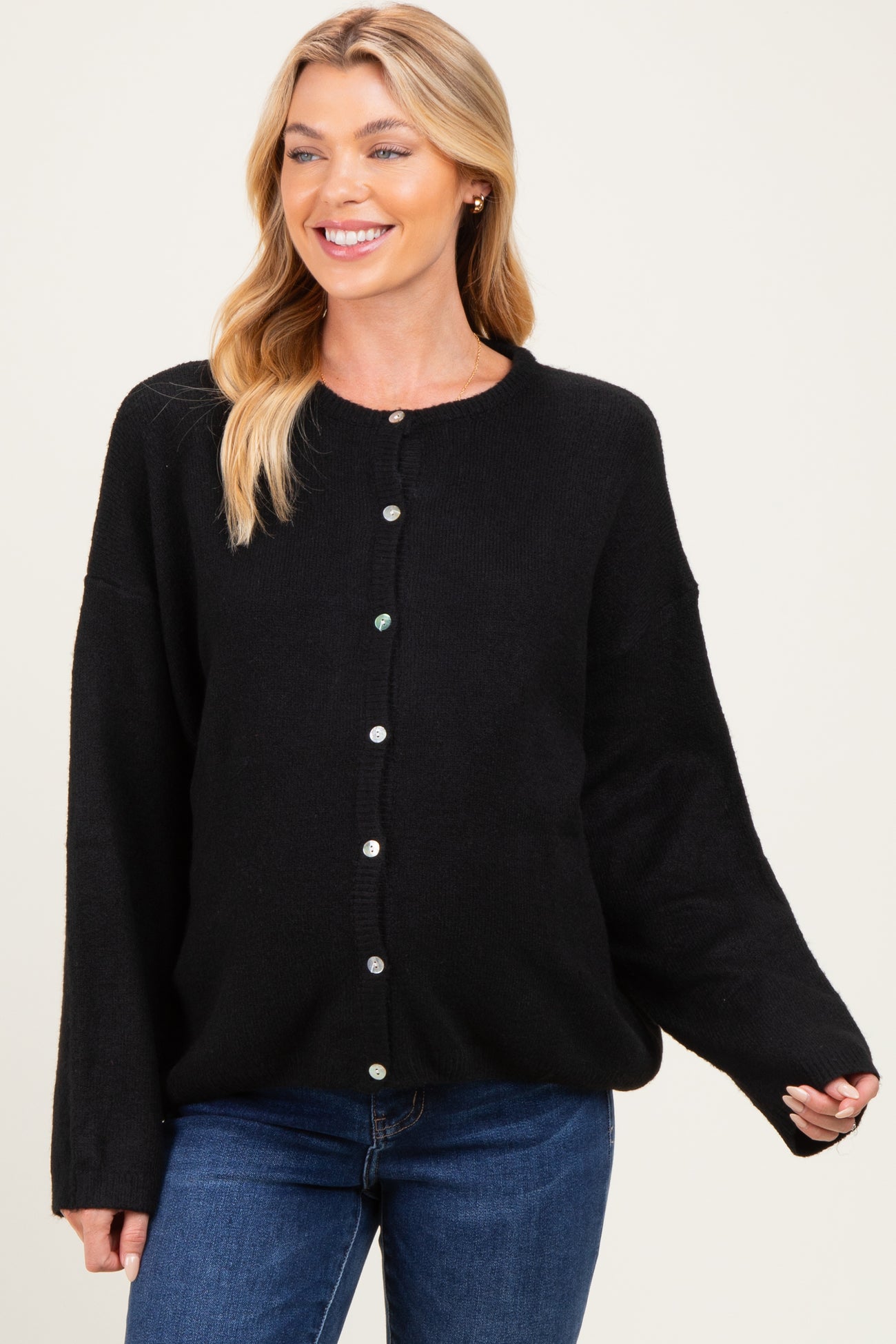 woman wearing a black oversized cardigan, smiling and showcasing her baby bump with blue jeans