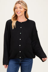 woman wearing a black oversized cardigan, smiling and showcasing her baby bump with blue jeans