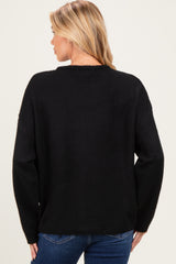 woman wearing a black loose-fitting maternity sweater, viewed from the back, paired with blue jeans