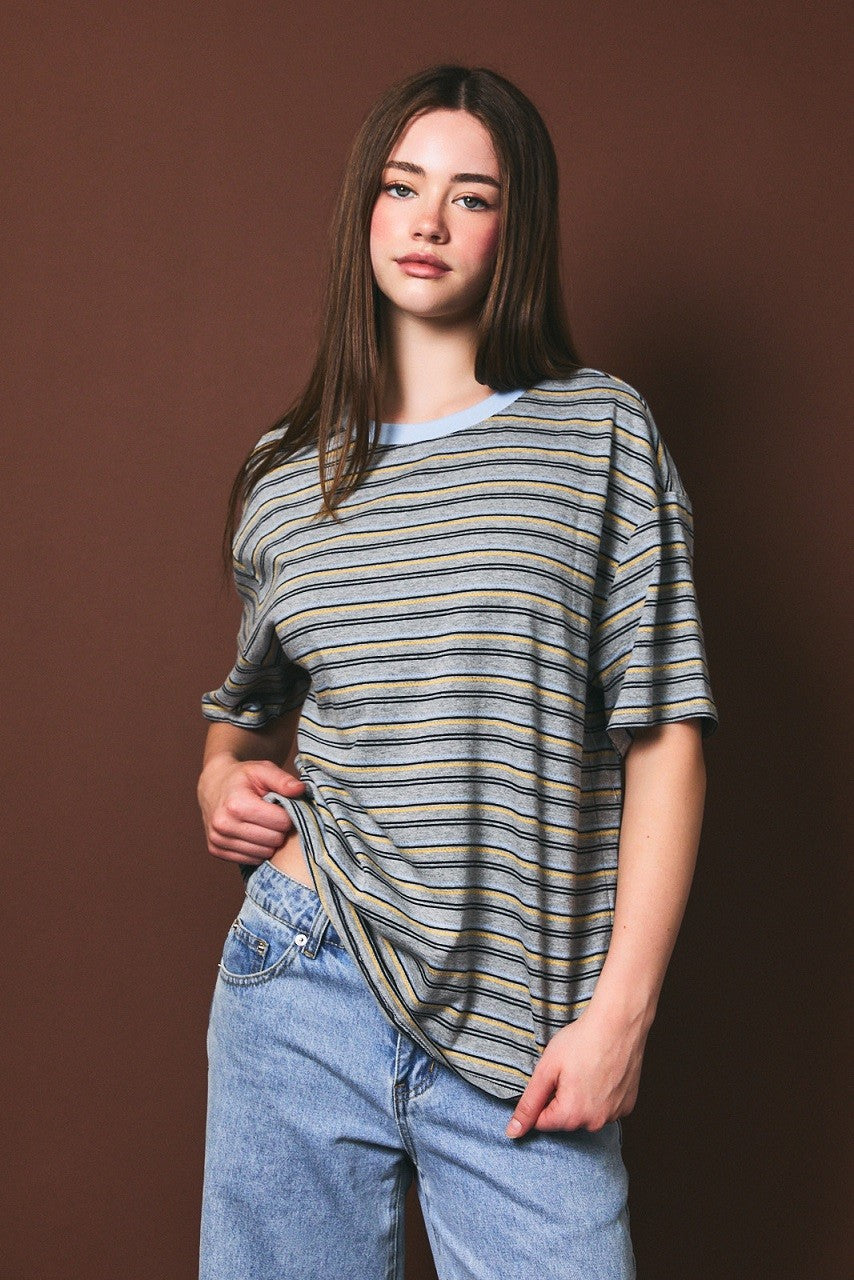woman wearing a striped oversized t-shirt in blue and beige with jeans against a brown background