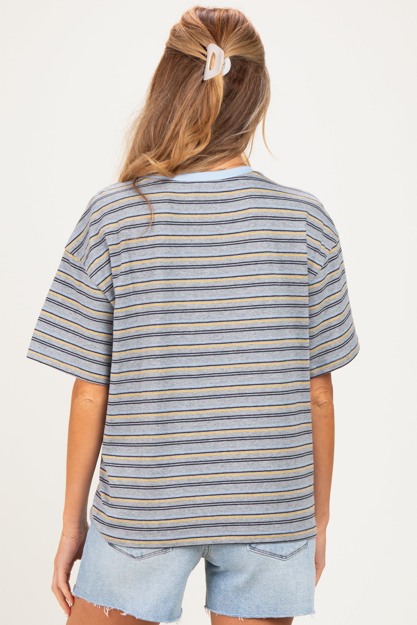 woman wearing a striped oversized maternity t-shirt with short sleeves and light blue denim shorts, showing her back