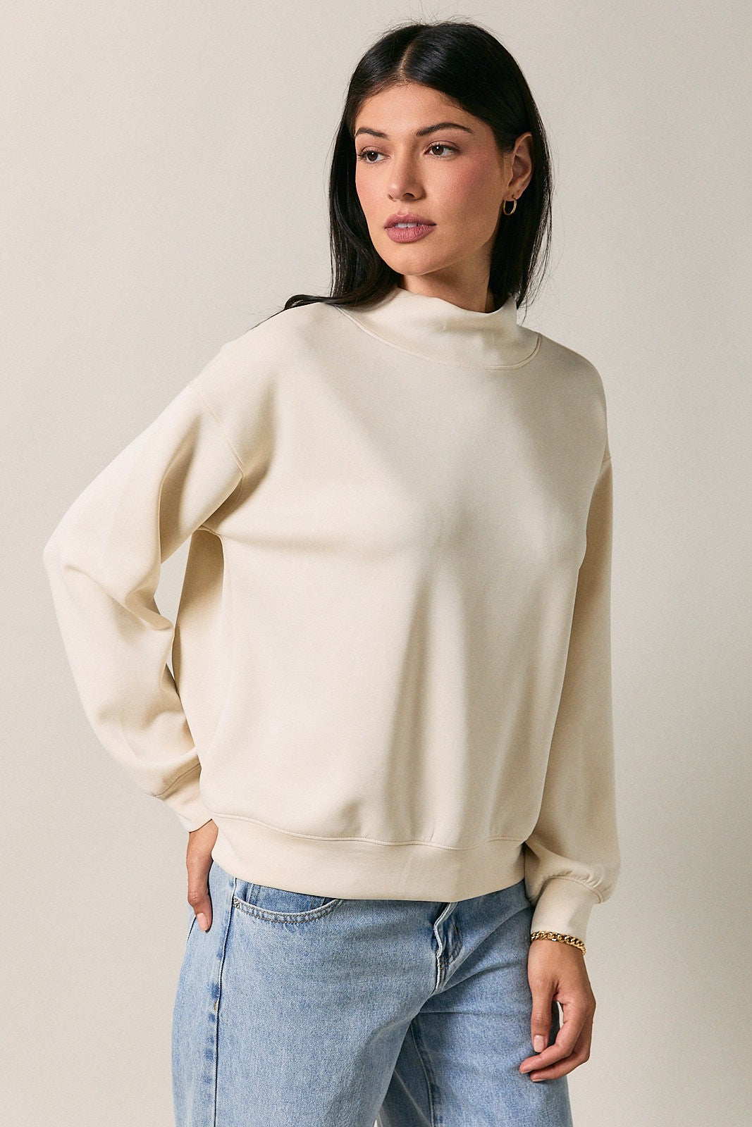 woman wearing a cream-colored mock neck sweatshirt with long sleeves and relaxed fit, styled with light wash jeans