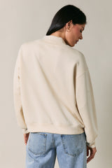 woman wearing a cream oversized sweatshirt with a simple crew neckline and dropped shoulder seams, styled with blue jeans