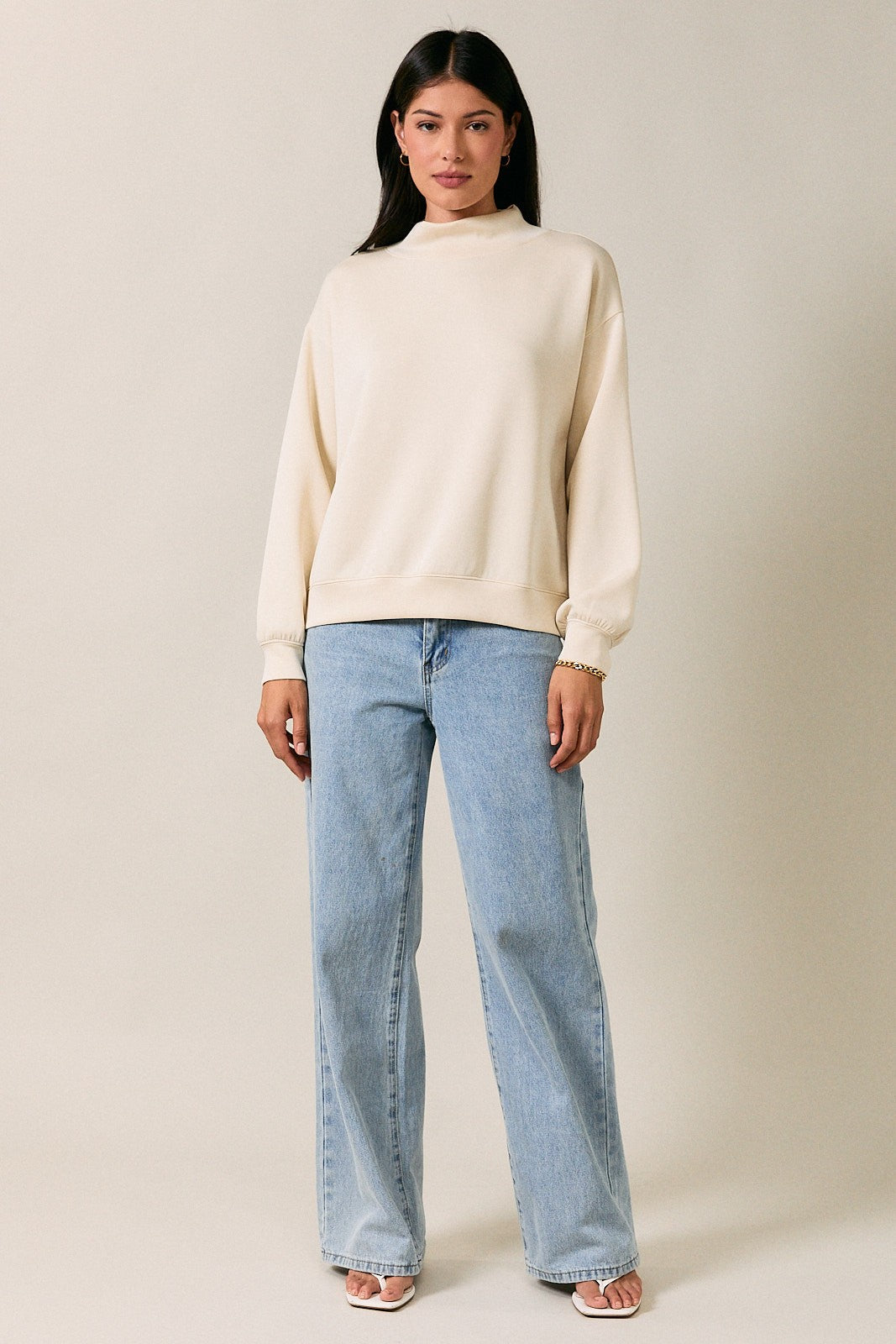 woman wearing a cream oversized sweatshirt with a mock neck and light wash wide leg jeans
