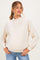 woman wearing a cream maternity sweatshirt with a high neck and balloon sleeves, showcasing her baby bump