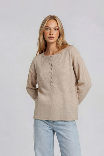woman wearing a beige long sleeve henley top with buttons and relaxed fit, paired with light blue jeans