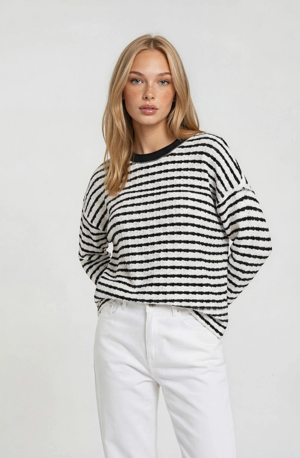 woman wearing a black and white striped sweater with long sleeves and a round neckline paired with white pants