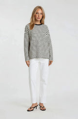 woman wearing a black and white striped sweater with long sleeves and white straight-leg pants