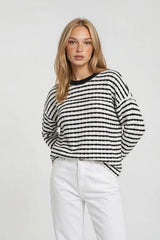 woman wearing a black and white striped sweater with long sleeves and a round neckline paired with white pants