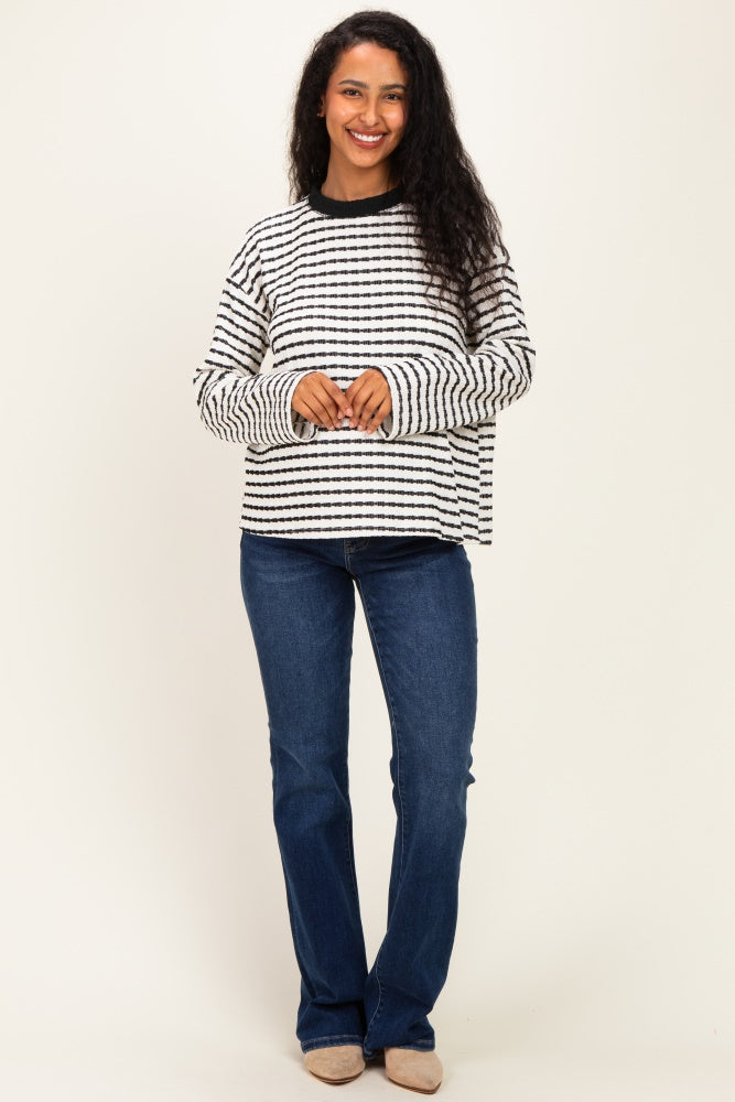 woman wearing a black and white striped maternity top with long sleeves and blue jeans, smiling at the camera