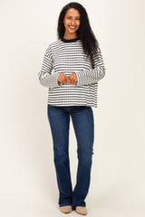 woman wearing a black and white striped maternity top with long sleeves and blue jeans, smiling at the camera