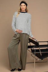 woman wearing a black and white striped maternity top and green wide-leg pants, showing her baby bump