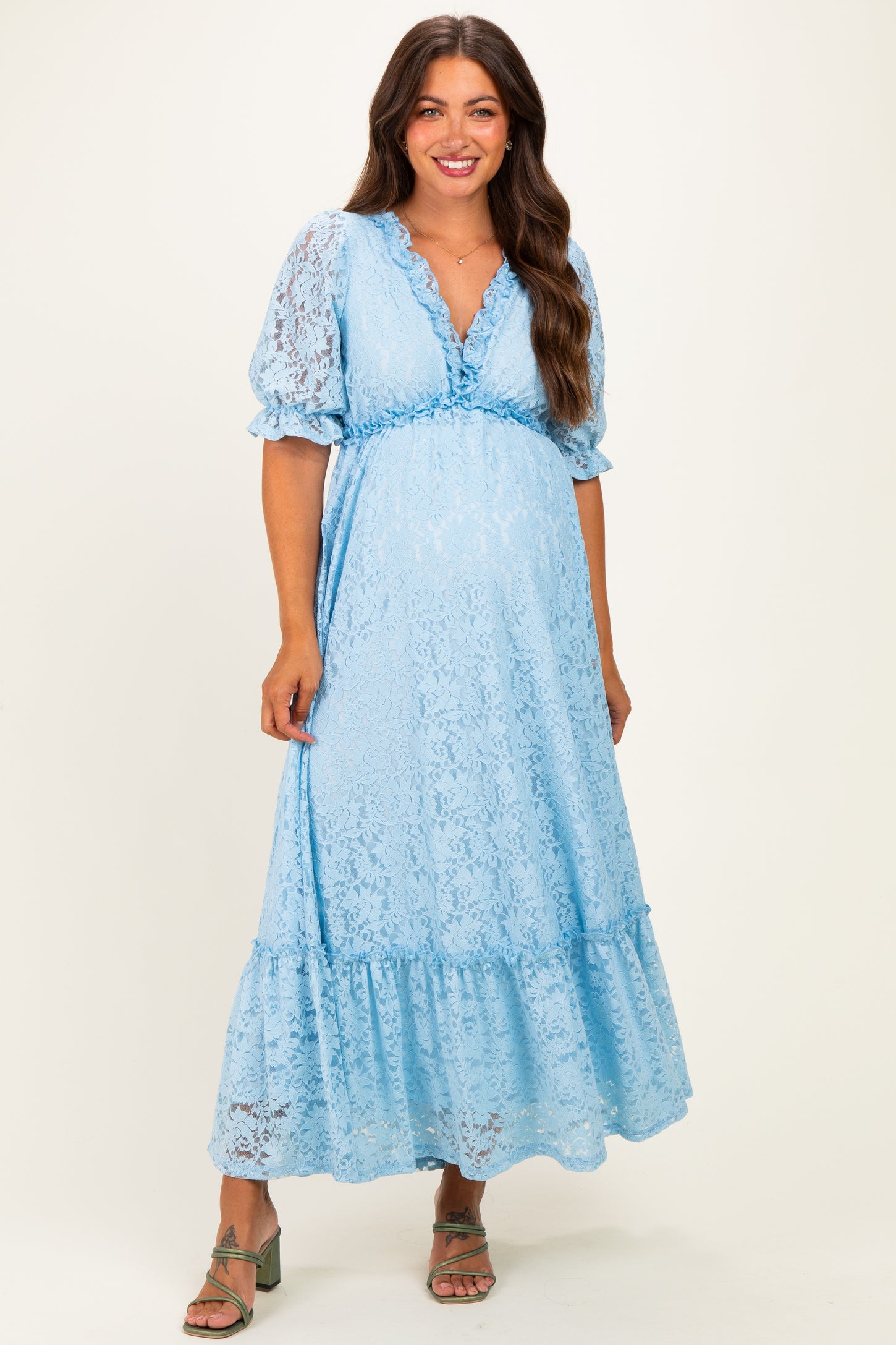 woman wearing a light blue lace maternity maxi dress with puff sleeves and a tiered hem, showing her baby bump