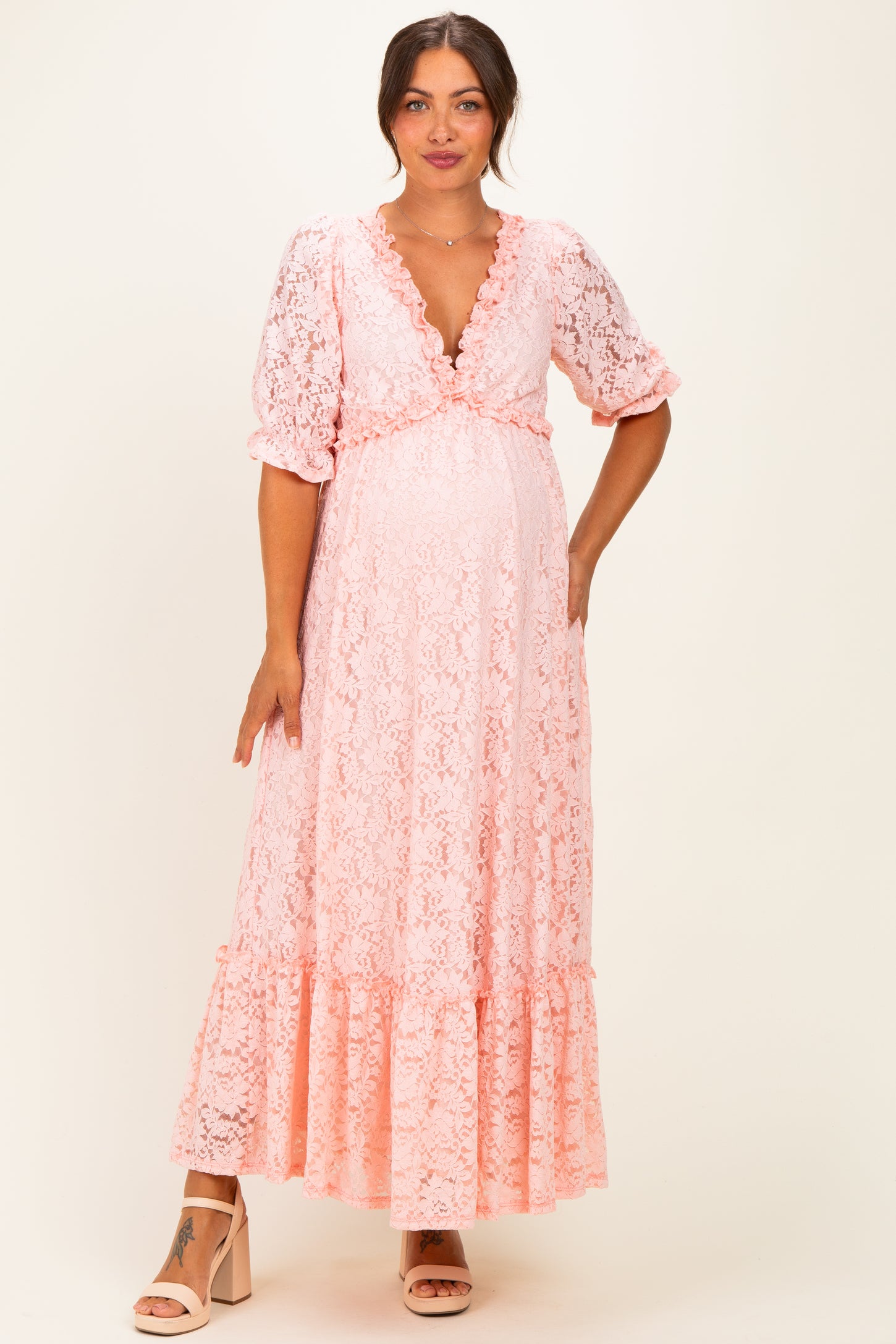 woman wearing a pink lace maternity maxi dress with a deep V-neck and ruffled sleeves, showcasing her baby bump
