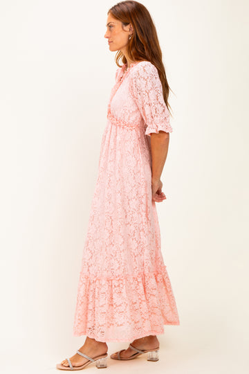 woman wearing a pink lace maxi dress with ruffled sleeves and a tiered skirt