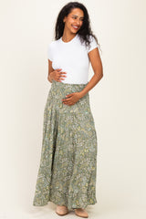 woman wearing a white short sleeve top and a long green floral maternity skirt, holding her baby bump