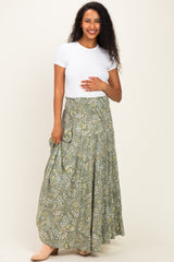 woman wearing a white short sleeve top and a flowy green floral maternity skirt, holding her baby bump