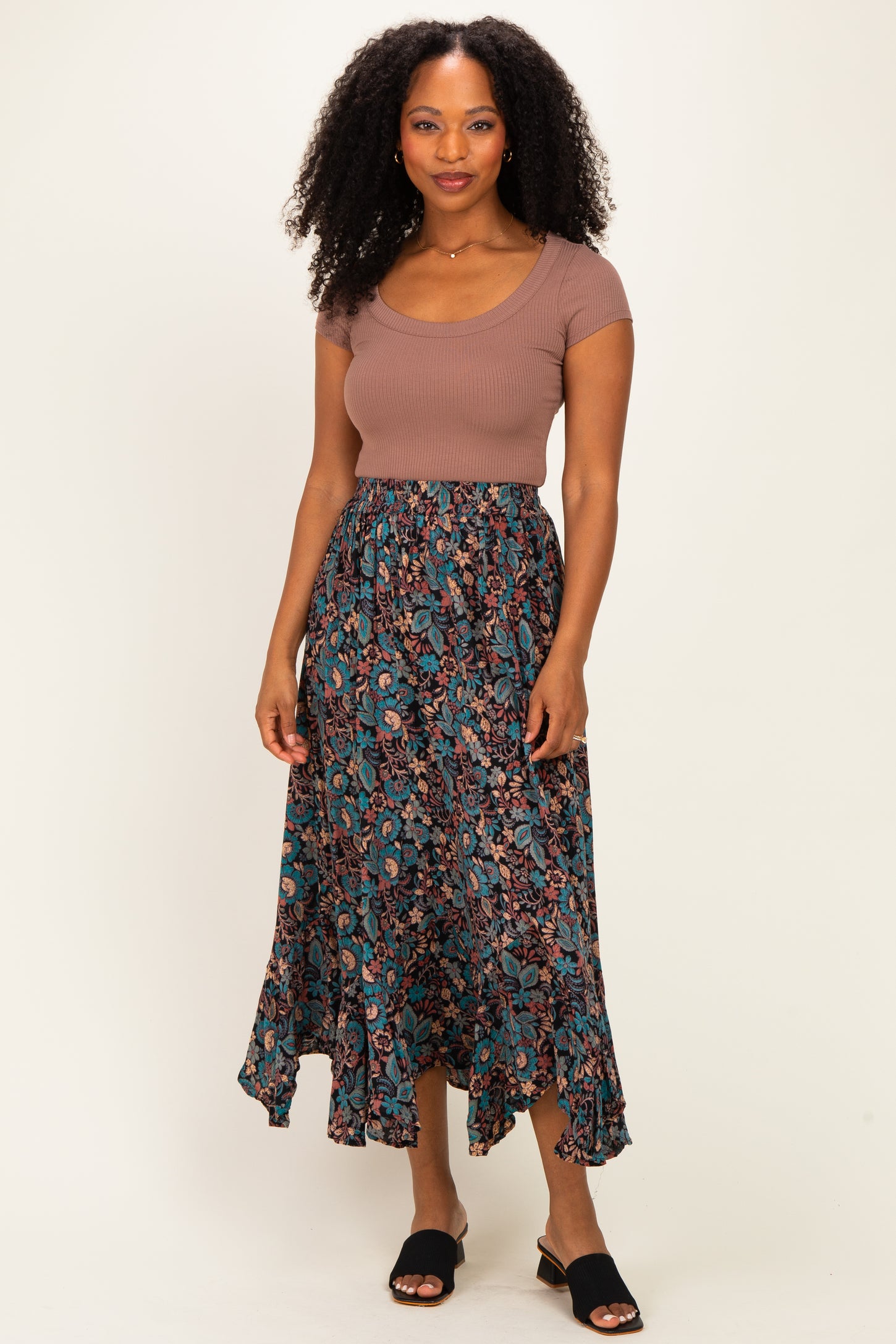 woman wearing a brown ribbed short sleeve top and a flowy teal floral maxi skirt with a high-low hem
