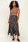 woman wearing a brown ribbed short sleeve top and a flowy teal floral maxi skirt with a high-low hem