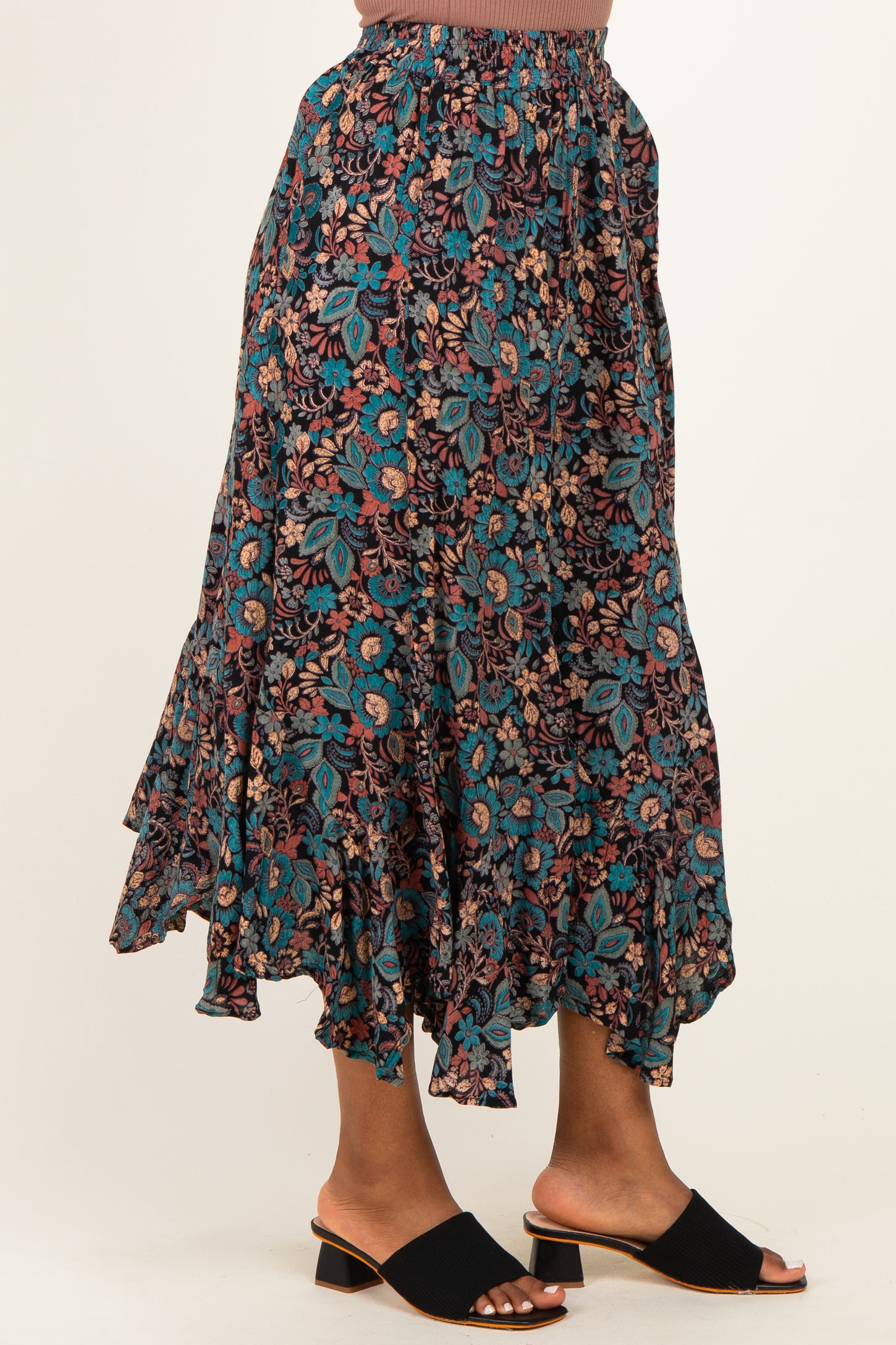 woman wearing a floral print tiered maxi skirt in teal and burgundy with a ruffled hem and black slide sandals