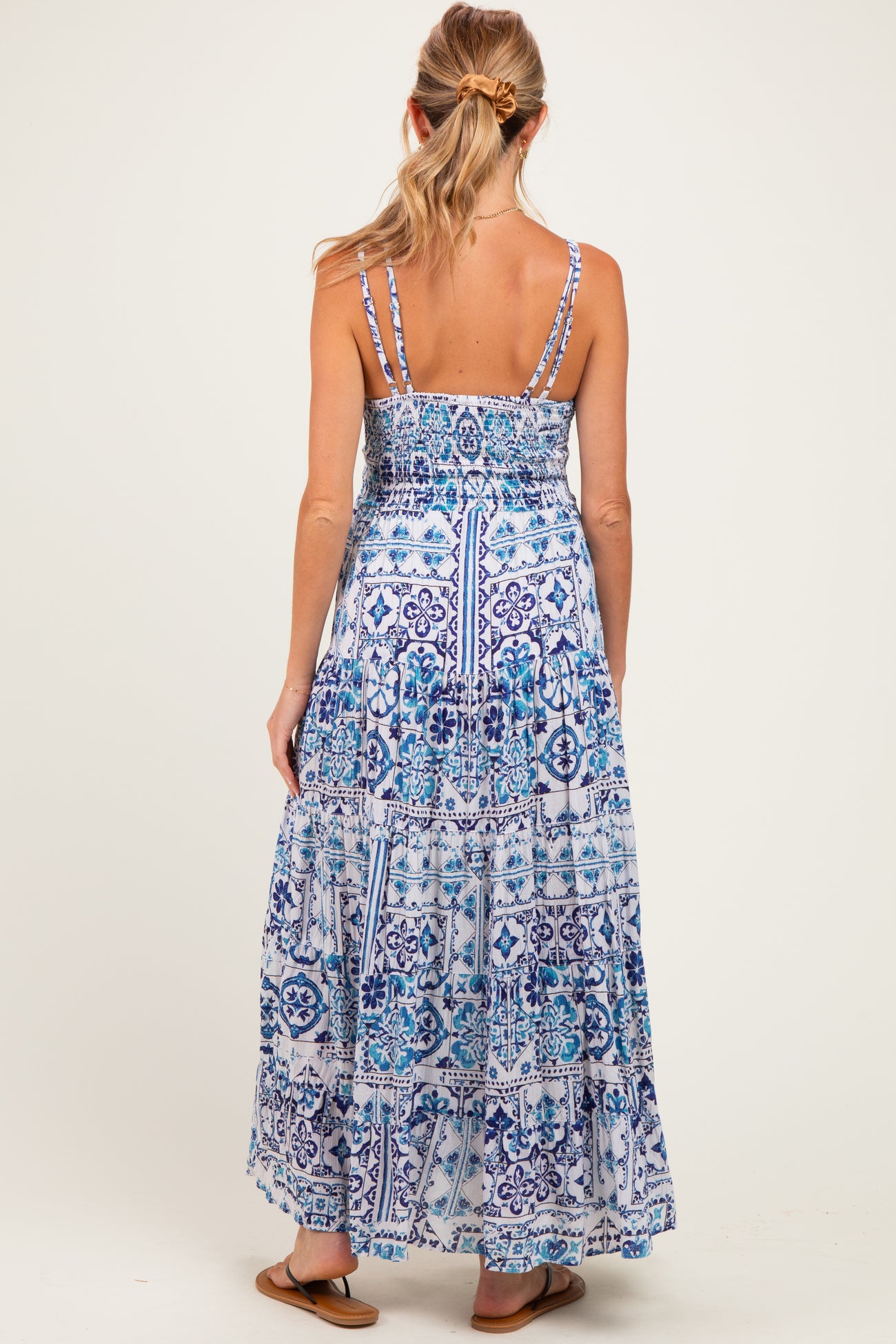 woman wearing a blue printed maternity maxi dress with spaghetti straps and tiered ruffle details, showing the back view