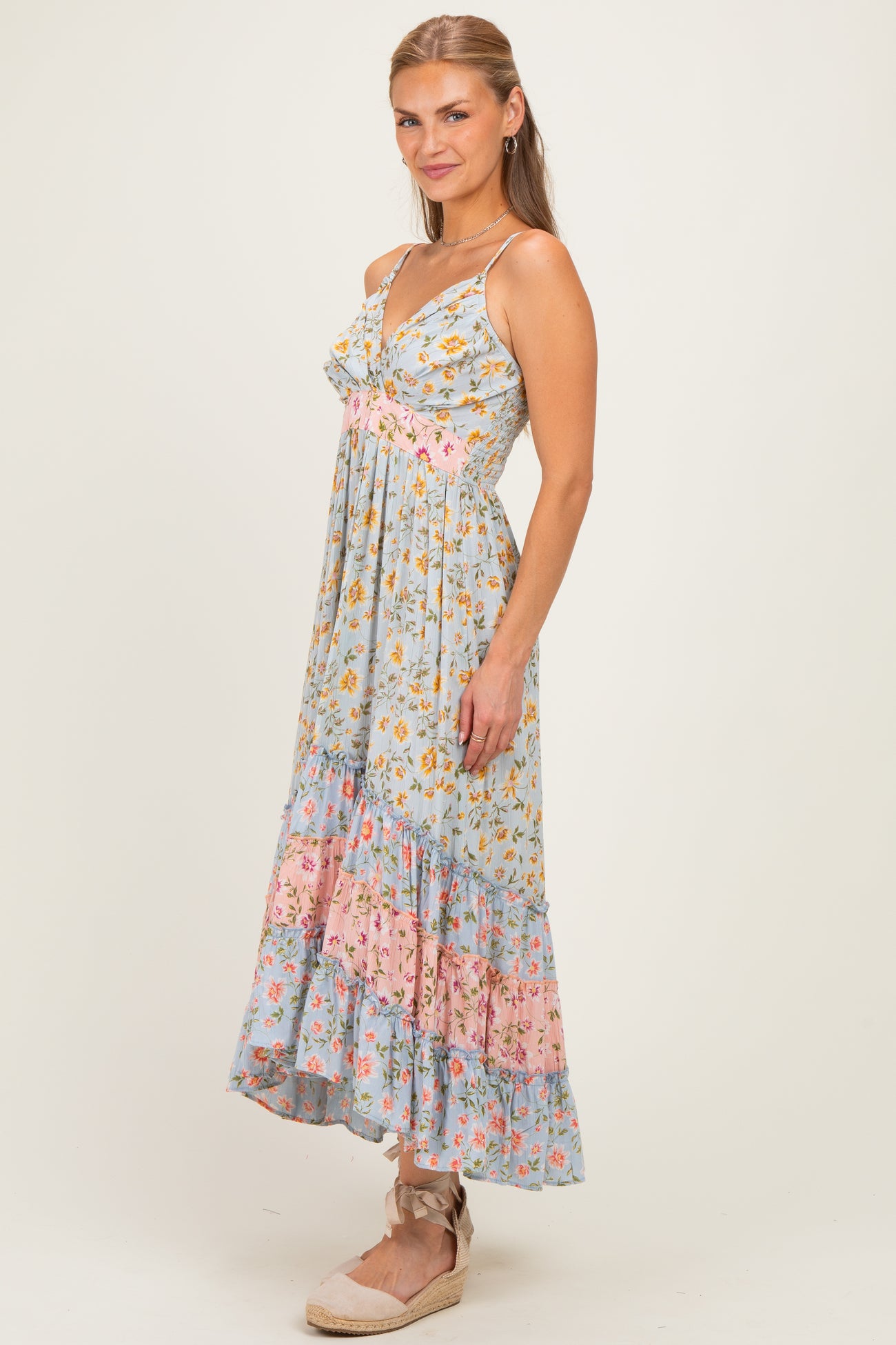 woman wearing a light blue floral maxi dress with pink accents and ruffled hem, standing against a neutral background