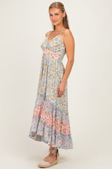 woman wearing a light blue floral maxi dress with pink accents and ruffled hem, standing against a neutral background
