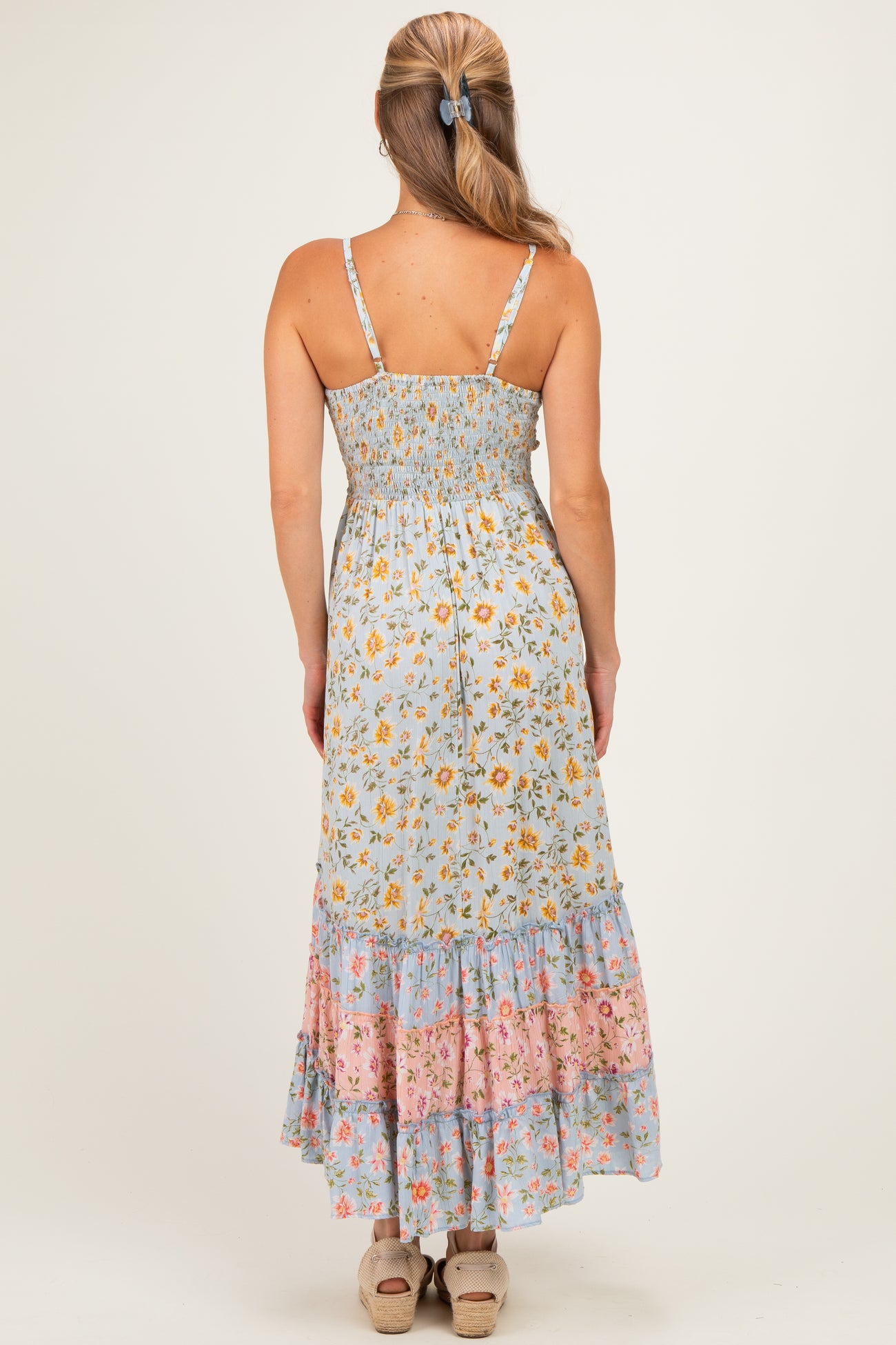 woman wearing a blue floral maxi dress with a smocked back and tiered hem, shown from the back