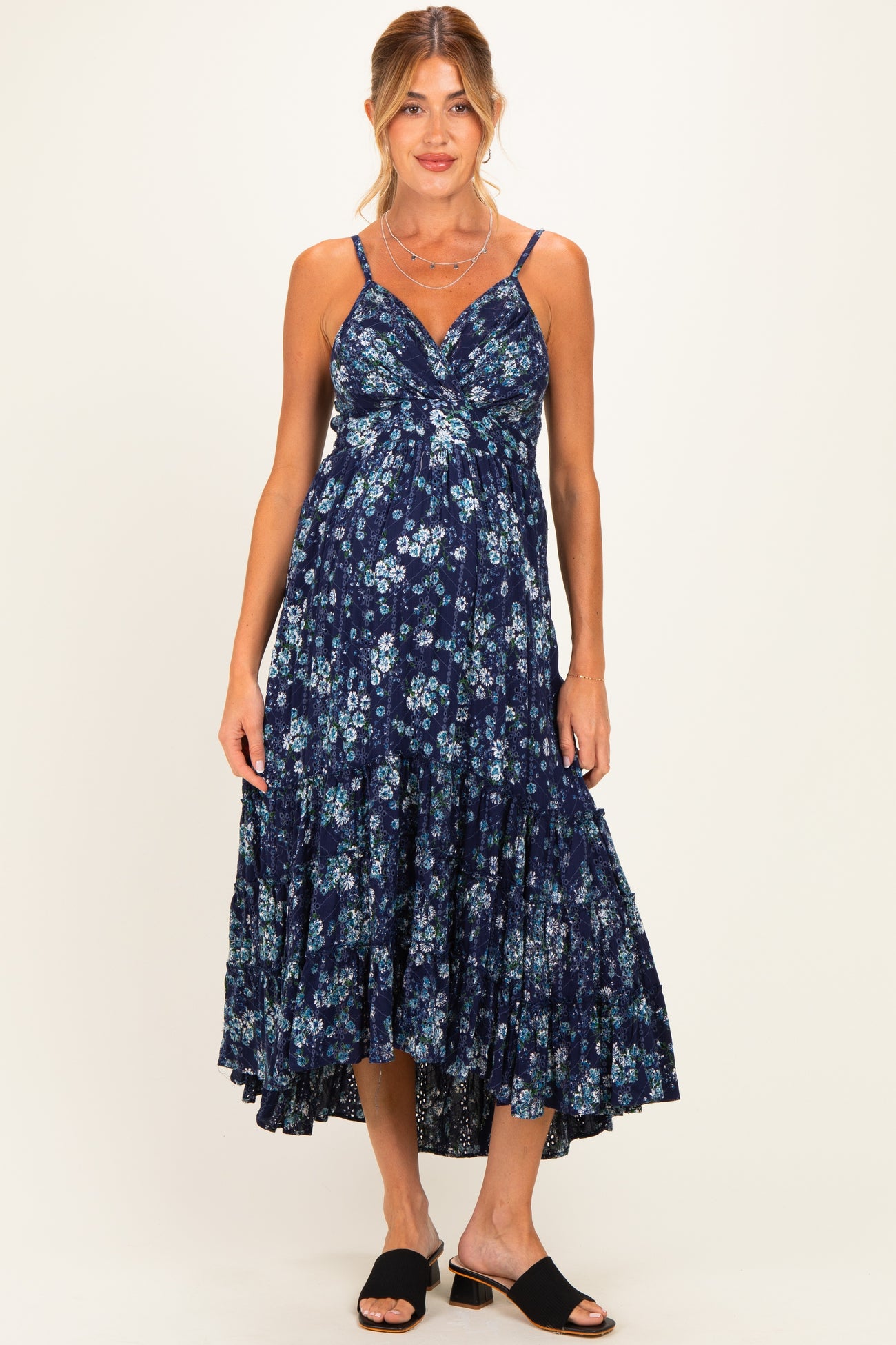 woman wearing a navy blue floral maternity dress with spaghetti straps and a tiered skirt, showing her baby bump